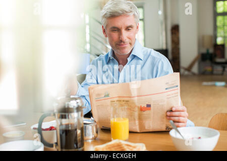Older man reading newspaper at breakfast table Stock Photo