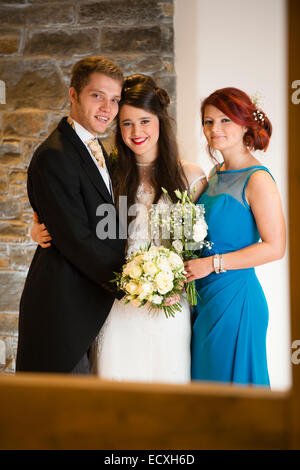 Getting married / Wedding day UK: the happy smiling bride and groom with the bridesmaid posing for photograph Stock Photo