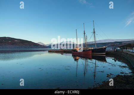 Commercial fishing boats sit in the harbour of Inverary on Loch Fyne.  Snow covers the peaks of the Scottish Highlands, Scotland Stock Photo