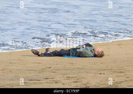 Man snoozing on beach is soaked by the incoming tide. Stock Photo