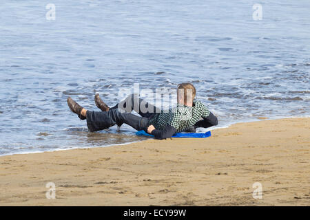 Man snoozing on beach is soaked by the incoming tide. Stock Photo