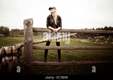 Caucasian woman standing on wooden fence at ranch Stock Photo