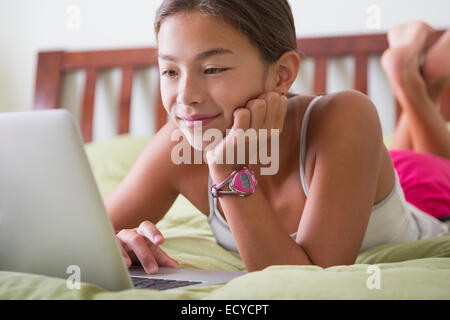 Mixed race girl using laptop on bed Stock Photo