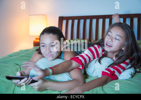 Mixed race sisters arguing about television on bed Stock Photo