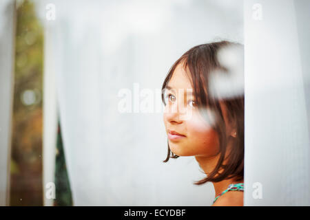 Mixed race girl standing near window Stock Photo