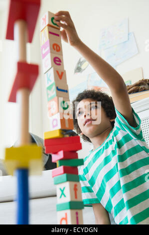 Mixed race boy building wooden block tower in living room Stock Photo
