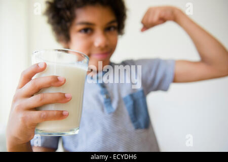 Mixed race boy flexing his muscle and drinking glass of milk Stock Photo