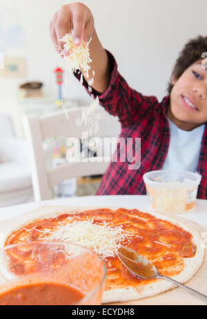 Mixed race boy sprinkling cheese on homemade pizza Stock Photo
