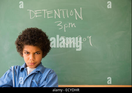 Angry mixed race boy frowning in classroom detention Stock Photo