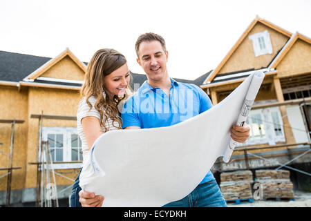 Caucasian couple reading blueprints outside house under construction Stock Photo
