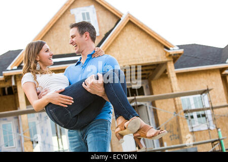 Caucasian man carrying woman near house under construction Stock Photo