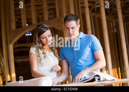 Caucasian couple reading blueprints in house under construction Stock Photo