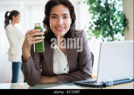 Hispanic businesswoman drinking green juice at desk in office Stock Photo