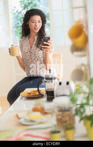 Mixed race woman using cell phone in kitchen Stock Photo