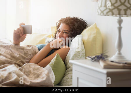 Mixed race woman using cell phone in bed Stock Photo