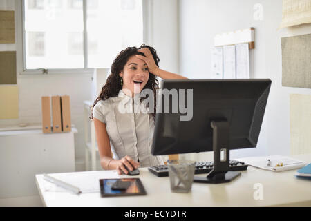 Mixed race businesswoman gasping at computer at desk in office Stock Photo