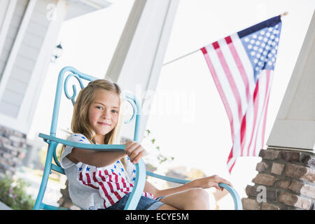 Caucasian girl sitting on porch near American flag Stock Photo
