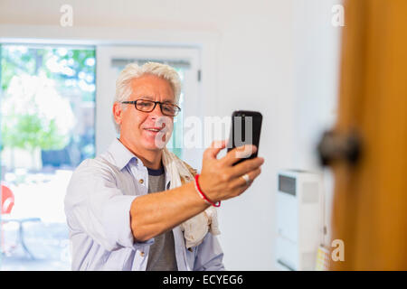 Older Hispanic artist taking cell phone photograph of art in studio Stock Photo