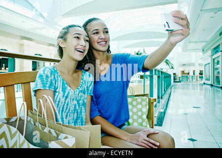 Mixed race teenage girls taking cell phone photograph at shopping mall Stock Photo