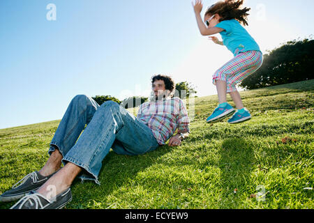 Girl jumping near father in grassy field Stock Photo