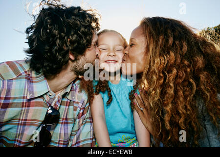 Parents kissing cheeks of daughter outdoors Stock Photo