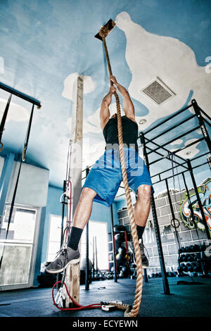 African American man climbing rope in gym Stock Photo