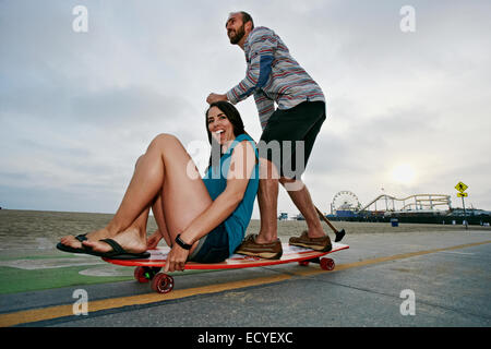 Caucasian couple skateboarding with paddle pole at beach Stock Photo