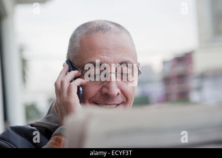 Hispanic senior man talking on cell phone and reading newspaper Stock Photo