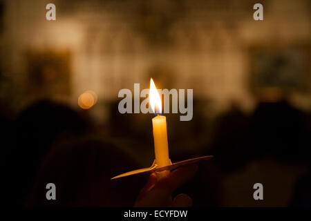 One 1 single lone candle light flame during a candlelit / lit Christian Church carol service Mass & congregation parishioners UK Stock Photo