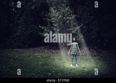 Mixed race girl standing in beam of light outdoors Stock Photo