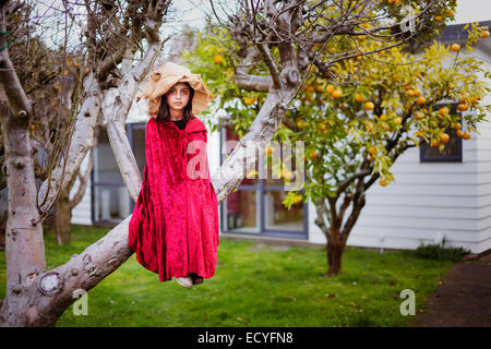Mixed race girl in witch costume sitting in tree Stock Photo
