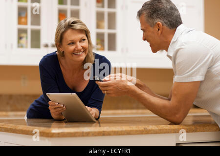 Caucasian couple using digital tablet and cell phone at kitchen counter Stock Photo