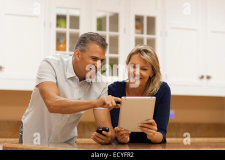 Caucasian couple using digital tablet and cell phone at kitchen counter Stock Photo
