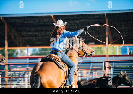 Caucasian cowgirl on horse throwing lasso in rodeo on ranch