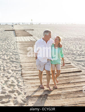 Caucasian couple walking on wooden boardwalk on beach Stock Photo