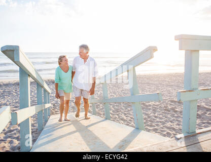 Caucasian couple walking on wooden boardwalk on beach Stock Photo