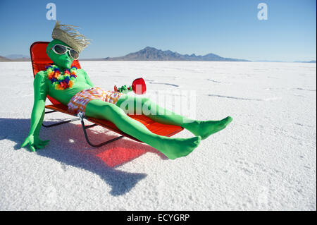 Funny drunk green alien tourist goes on cheap holiday relaxing in beach chair with tropical drink Stock Photo