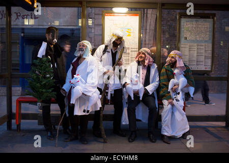 Work colleagues in fancy dress for their Christmas party, dressed up as three / four wise men, wait at a bus stop in London, UK. Stock Photo