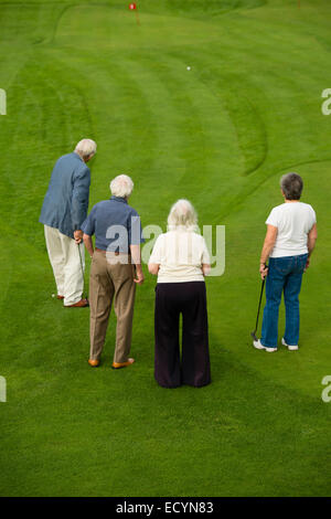 A group of 4 four seniors, retired couples, pensioners, on holiday vacation playing miniature golf, UK Stock Photo