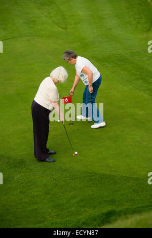 Two senior women retired, pensioners, on holiday vacation playing miniature golf, UK Stock Photo