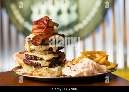 A monster multi-layered high-calorie fattening huge meal of 4 four hamburgers cheeseburgers  beef burger patties, fried  bacon, melted cheese and chips french fries, UK Stock Photo