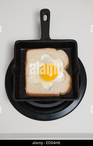 Fried egg in a hole cooking in a toasted bread slice in a black cast iron skillet. Traditional breakfast toad in the hole or bird's nest, top view. Stock Photo