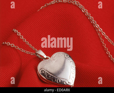 Ladies silver locket on chain against red material. Stock Photo