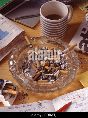 A cup of coffee and a glass ashtray with a cigarette on a wooden table.  Coffee drink. A cigarette in an ashtray. Wooden table. Hot drink. Street  Cafe Stock Photo