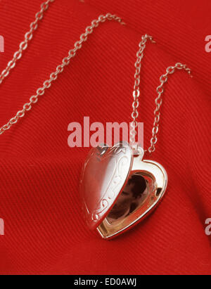 Ladies silver locket on chain against red material. Stock Photo