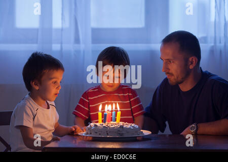 Boy about to blow out candles on his birthday cake  with his father and brother Stock Photo