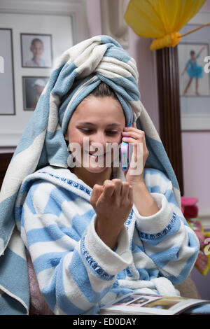Girl in dressing gown talking on her mobile phone while looking at her nails Stock Photo