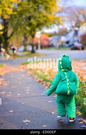 Boy in dinosaur costume walking on sidewalk Stock Photo