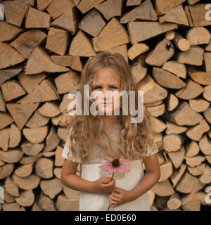 Portrait of girl (4-5) with pink flower against stack of logs Stock Photo