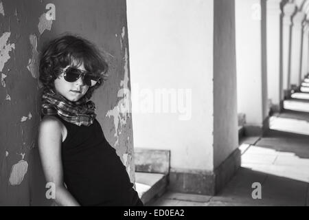 Boy (6-7) leaning against wall and looking at camera through sunglasses Stock Photo